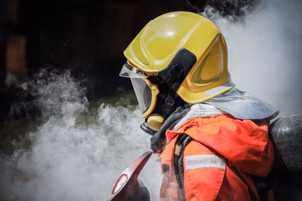 A firefighter in full protective gear surrounded by heavy smoke, illustrating the urgent need for professional smoke remediation services after a fire.